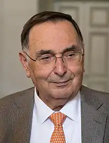Gian Paolo Dallara wearing a Tan blazer, white buttoned-up shirt and a orange tie