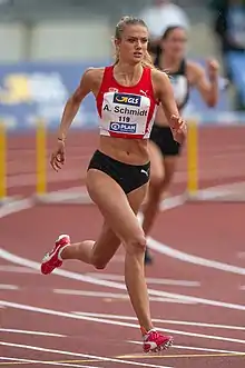 Blonde woman in a red top and black short running on a red track