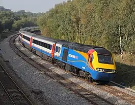 Engine with passenger carriages approacing on a left turn flanked by a stand of trees taken from an overbridge