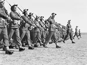 Black and white photo of a large group of men wearing military uniforms and carrying rifles marching in close formation