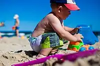 Image 28An infant boy playing with a toy dump truck at the beach. (from Boys' toys and games)