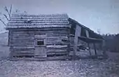 A log cabin with some logs missing and a lean-to attached to its side