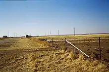 A view across a western Oklahoma field, with some broken foundations and grain storage bins.