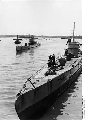 Black and white photograph of two World War II-era submarines on the surface of the sea. Land is visible in the background.