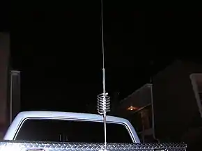 A tall antenna with a helical coil in the middle, mounted on pickup-truck metal tool box