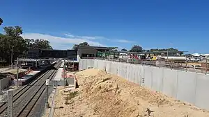 View from a bridge of a dual-tracked railway line with concrete retaining walls and a metal concourse under construction