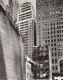 Old tenements with laundry from clotheslines are contrasted with imposing new skyscrapers