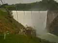 Englebright Dam during spring floods.  Water is spilling over the dam's crest.  Narrows II Powerhouse is visible at the base of the dam.