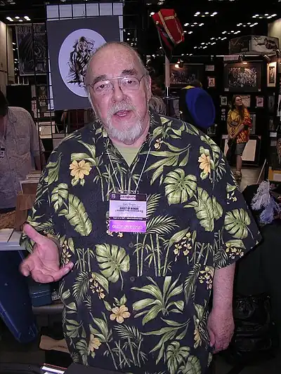 A man in his late sixties. He has a beard, glasses, and is wearing a Hawaiian shirt.