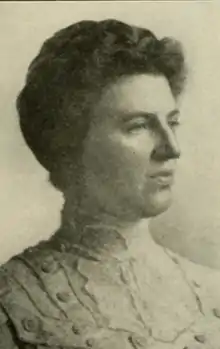 A white woman with dark hair dressed back to the nape, wearing a lacy high-collared shirtwaist or dress