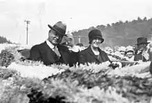 Herbert and Lou Henry Hoover sitting together in the back of an open-top car as a crowd looks on