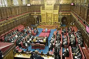 Wood-panelled room with high ceiling containing comfortable red padded benches and large gold throne.