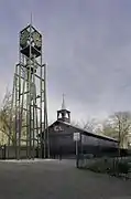 Houten zaalkerk met op de voorgrond een vrijstaande stalen klokkentoren - Koedijk