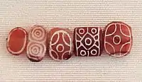 Indus carnelian beads with white design, etched in white with an acid, imported to Susa in 2600โ1700 BC. Found in the tell of the Susa acropolis. Louvre Museum, reference Sb 17751. These beads are identical with beads found in the Indus Civilization site of Dholavira.
