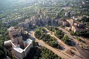 Freedom Square, Kharkiv in 2003, showing half of the square area (only the circular neighbouring park on the north-western edge). The square proper begins at the large statue of Lenin (this statue has since been removed). This statue of Lenin is seen in the lower right corner, casting a long shadow which points into the square.