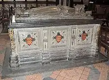 A photograph of the tomb of King John; a large carved, square, stone block supports a carved effigy of the king lying down.