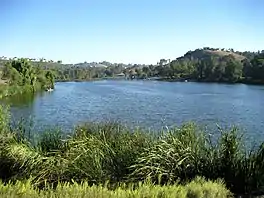 A light-blue reservoir formed by a large dam across a broad valley ringed by houses