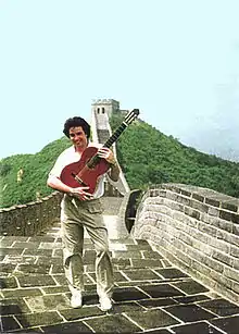 Laucke holding guitar and smiling, standing on top of the Great Wall of China
