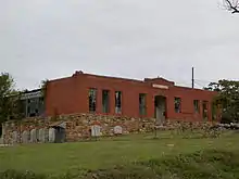 A red brick building with broken windows and lots of vegetation.