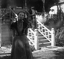 Lou Henry Hoover as a young woman standing in front of the porch of a house