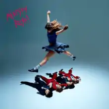 A girl jumping over the four members of Måneskin lying on the ground