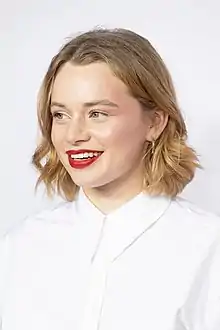 Luna Wedler wearing white, smiling and looking right of the camera
