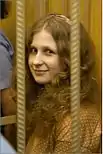 A woman with strawberry blonde curly long hair smile toward the camera. The photo is obstructed by two bars of a very small cell.