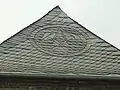 Slate roofers guild emblem as an ornament made with slate roof shingles, Meerbusch, Germany. Note the hip shingles act as a ridge cap.