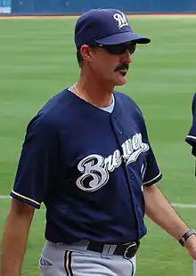 A thin, mustachioed man wearing a navy blue baseball cap and jersey