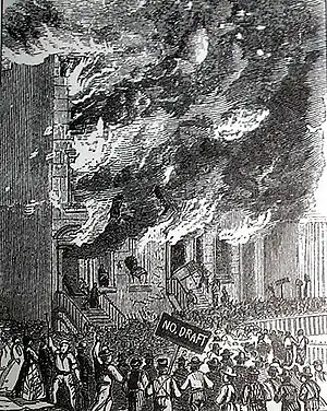 Building on fire as rioters look on, one holds a sign that says "no draft"