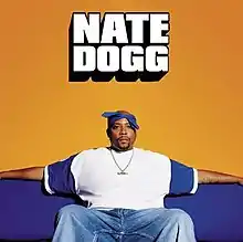 A man wearing a blue-and-white t-shirt, blue jeans and bandana is sitting on a blue couch.