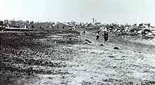In the distance a group of people walk down a dirt road away from the village.
