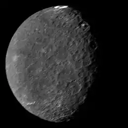 A round spherical body with its left half illuminated. The surface is dark and has a low contrast. There are only a few bright patches. The terminator is slightly to the right from the center and runs from the top to bottom. A large crater with a bright ring on its floor can be seen at the top of the image near the terminator. A pair of large craters with bright central peaks can be seen along the terminator in the upper part of the body. The illuminated surface is covered by a large number of craters.