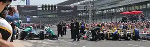 Two sets of racing mechanics fitting tires to two separate racing car and simulating the insertion of fuel in the racing vehicles