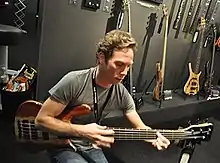 Young man playing bass in front of a display of other guitars