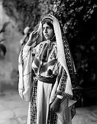 Image 10A young woman from Ramallah, c. 1898-1914. Until the 1940s, women of Palestine wore elaborate handcrafted garments. The creation and maintenance of these items played a significant role in their lives. A knowledgeable observer could determine a woman's village of origin and social status from her clothing. The circular band near this woman's forehead is a ring of coins made from a portion of her dowry money, and indicates that she is unmarried.'Ali Ra'if Efendi, (edited by Durova)