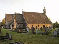 A church seen from the north with an extensive roof.  On the right is the nave with a bellcote at the west end; on the left is the chancel with the vestry.