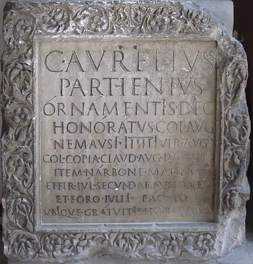 A parallelpiped of stone with a Latin inscription and a floral border.