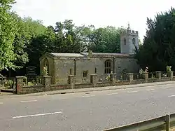 A stone church with a tower on the right.  This has a battlemented parapet beyond which is a small pyramidal roof.