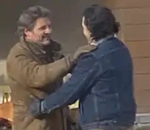 Two men with dark hair, both wearing thick jackets, embracing each other.
