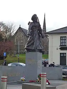 a bronze sculpture of man wearing a Sikh turban and carrying a rifle on his left side, set on a granite plinth on in a small plaza
