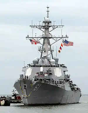 A grey ship with flags flying arrives in port