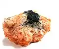 A lustrous, black, octahedral crystal of uraninite on orange calcite, from Bancroft