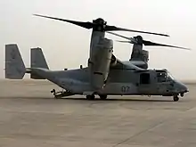  A side view of an MV-22 resting on sandy ground with its ramp lowered.