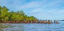 Dozens of warriors with staffs in canoes