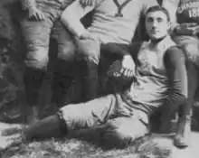 A greyscale image of a man in a football uniform resting his arm on someone's knee