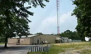 A one-story metal building with a W L I W logo next to the base of a tall broadcasting tower